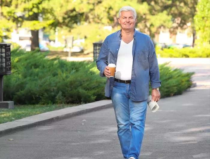 older man walking down street with coffee and paper