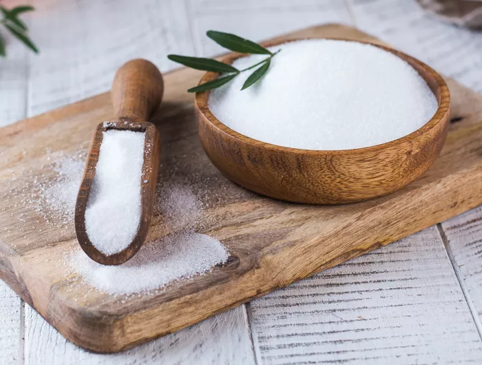 bowl and scoop filled with sugar on wood cutting board