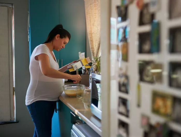 Pregnant woman holding mixing bowl with batter and reading the back of a corn masa flour box