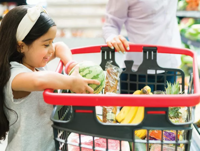 Young girl placing produce into a shopping cart