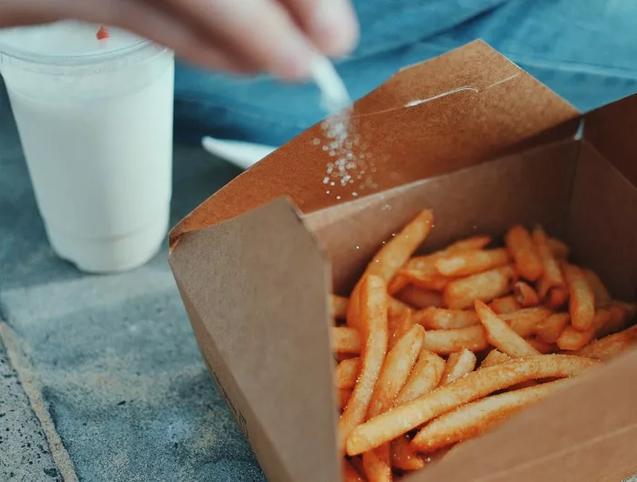 A person sprinkling extra salt on their fast food fries