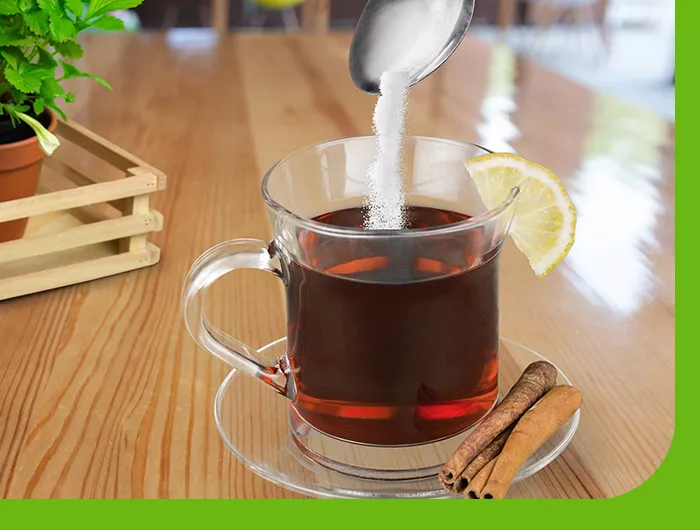 clear mug holding tea pouring sugar into