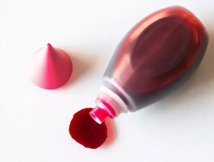 a bottle of red dye spilling onto a white surface