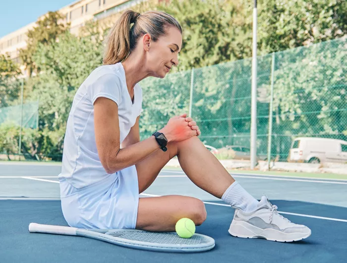 woman sitting on tennis court holding her knee