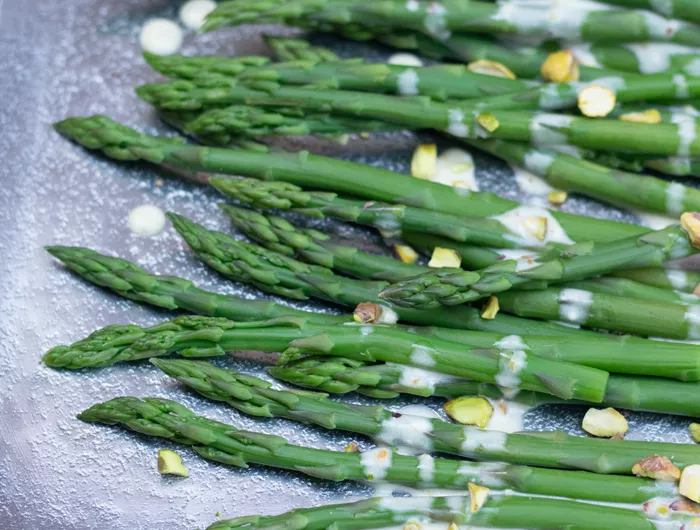 cooked asparagus covered in sauce and pistachios