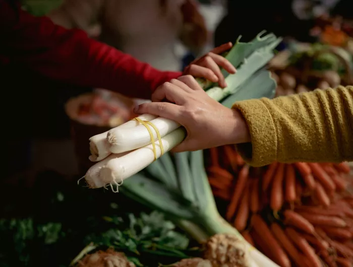 A woman buying leeks from a fresh produce stand