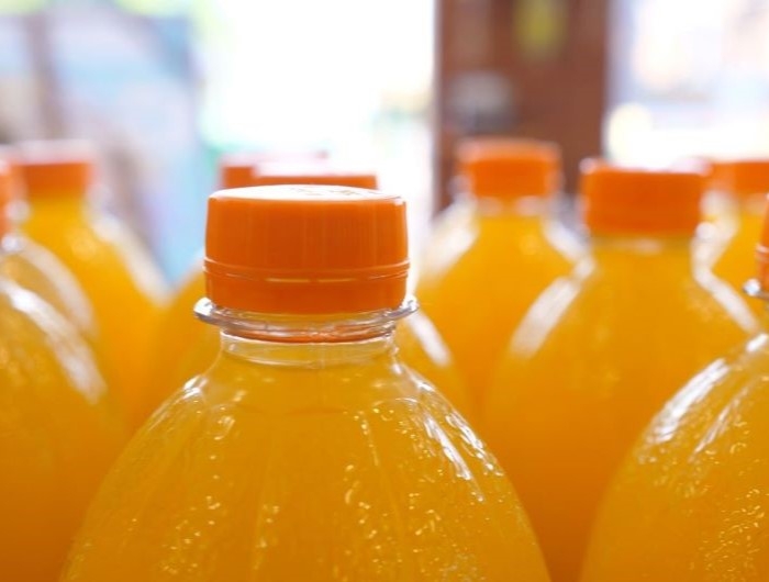 Close up of top parts of orange soda in plastic bottles on a display in a supermarket