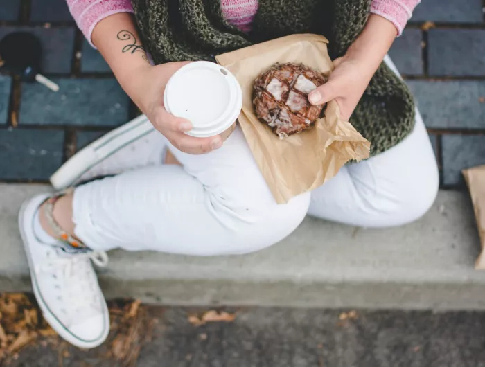 A person holding a coffee drink and a glazed pastry