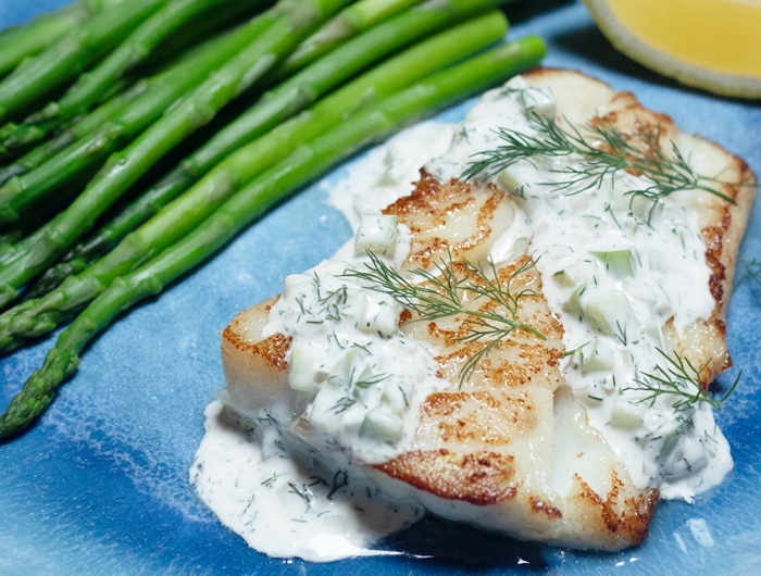 piece of white fish covered in tartar sauce with some asparagus on a plate