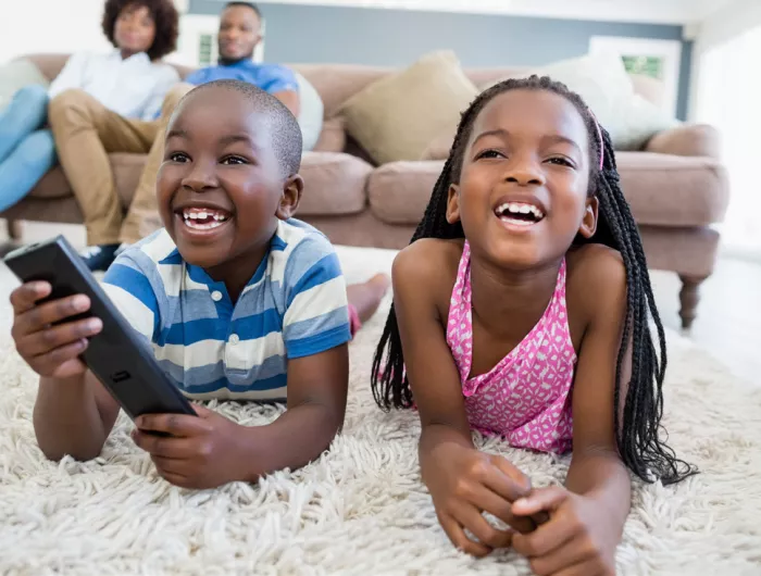 Two young children watching TV from the carpet, with their parents on the couch behind them