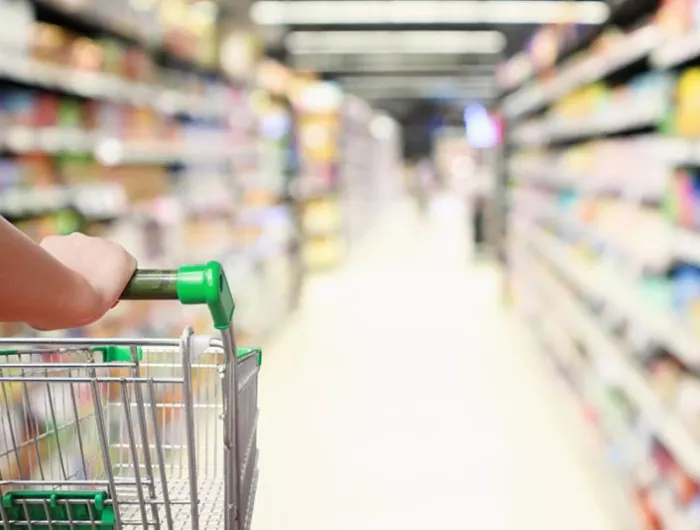 A shopper with grocery cart looking down a long supermarket aisle