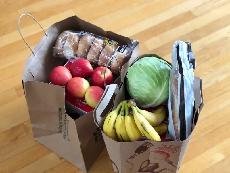 Two paper grocery bags full of apples, bananas, cabbage, and bread products