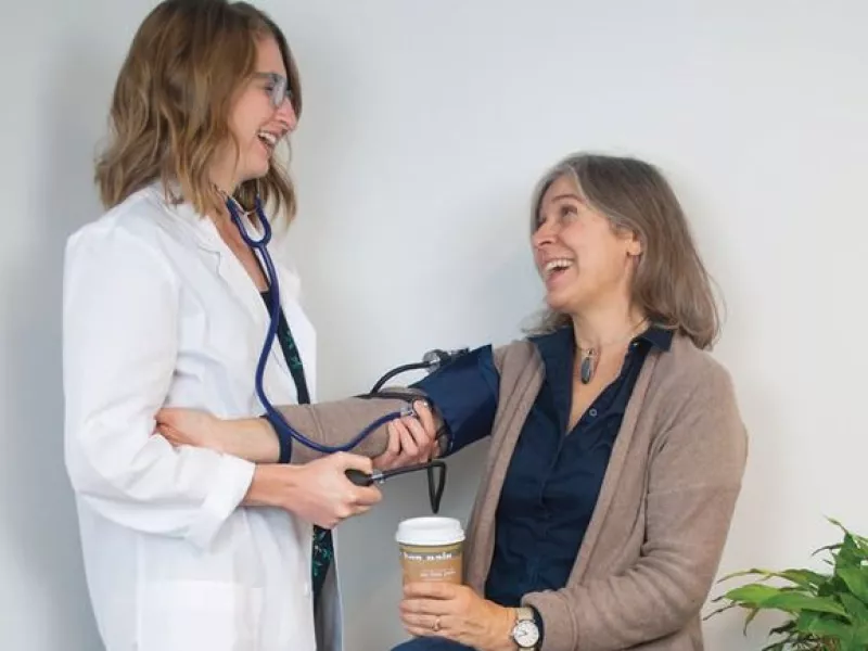 woman in a white coat taking a blood pressure reading from another woman, seated