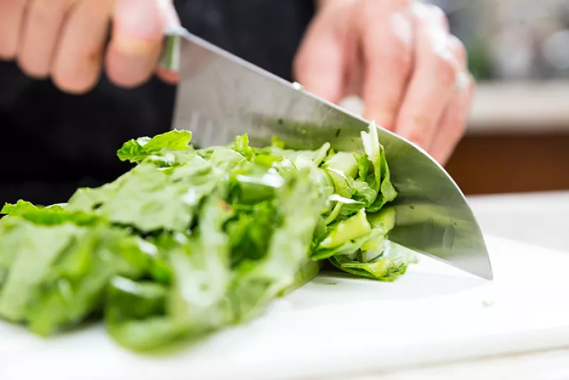 hands holding a knife and chopping romaine lettuce