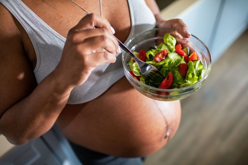 Young pregnant latine woman eating a salad in the kitchen of a home