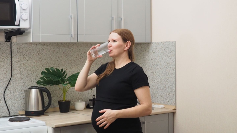 pregnant woman drinking water in the kitchen