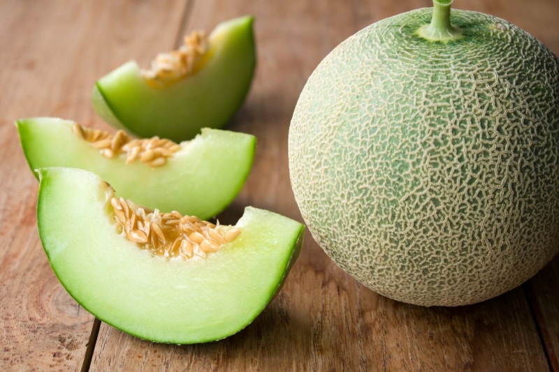 Fresh honeydew melon, whole and sliced into wedges, on a wooden surface