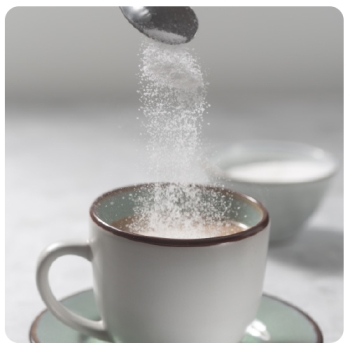 spoon pouring sugar into cup of coffee on a green saucer