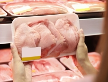 person holding a package or raw chicken in front chicken shelf at supermarket